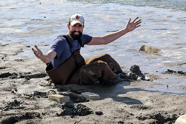 person sits in the sand near the water's edge